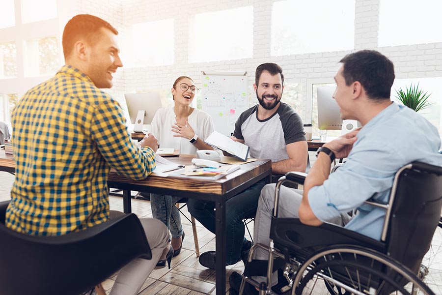 Employee Benefits - Group of Coworkers Sit at a Conference Table Laughing and Collaborating on Their Work